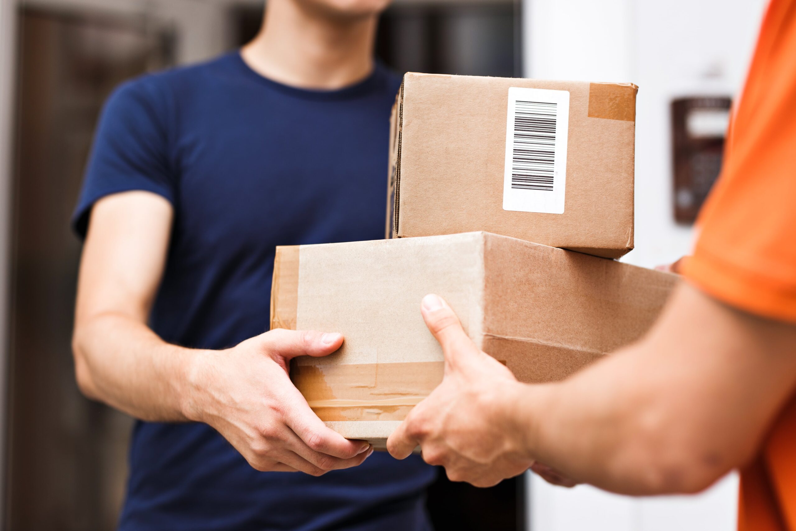 A picture of a delivery man handing another man two boxes.