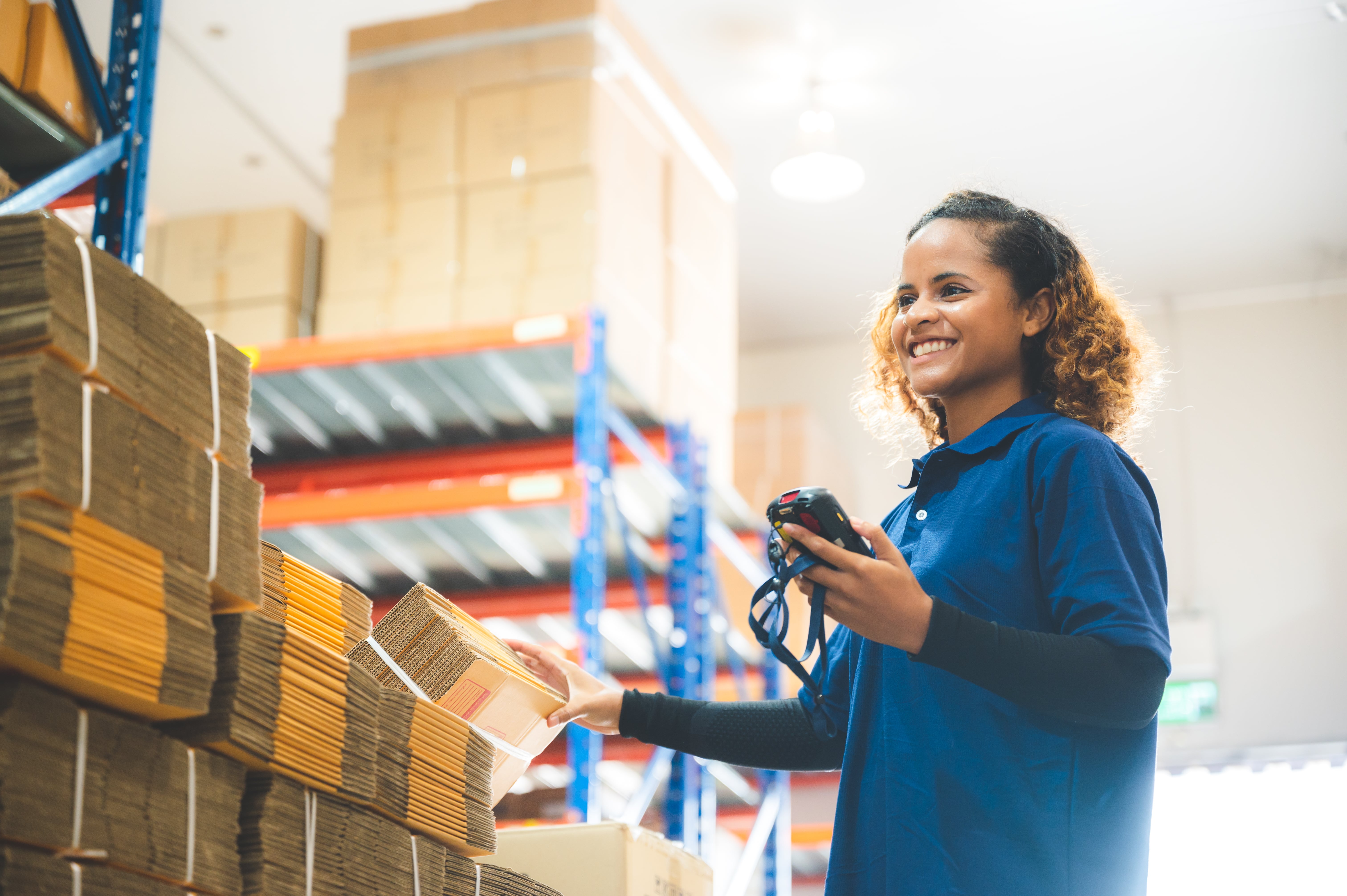 A warehouse worker wearing a blue polo scanning inventory and smiling.