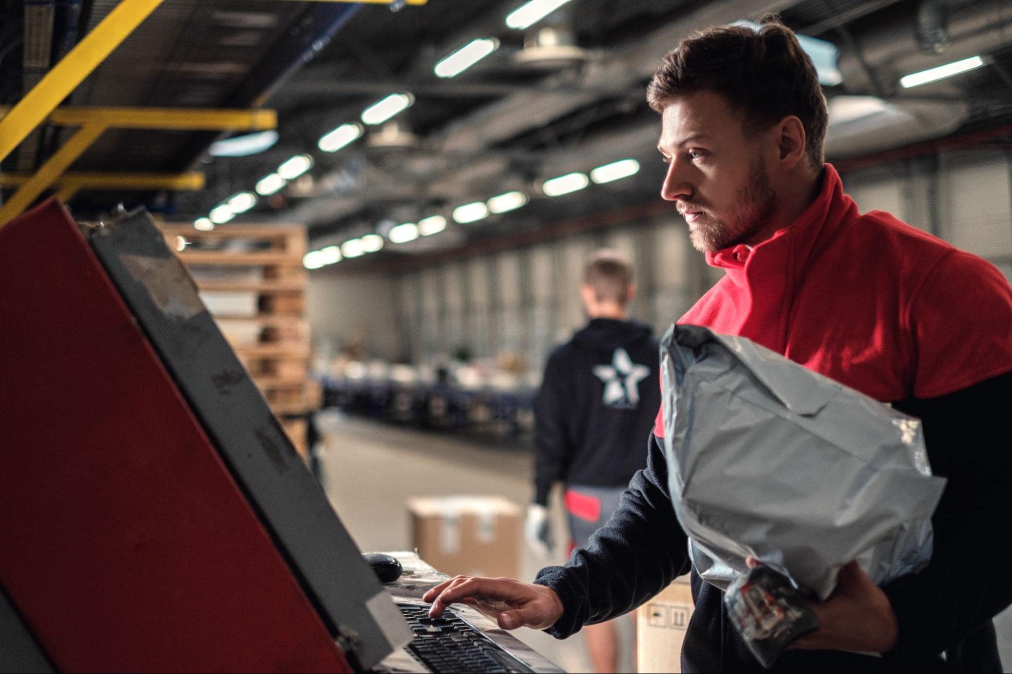 A warehouse worker holding a package and adding information to a warehouse computer.