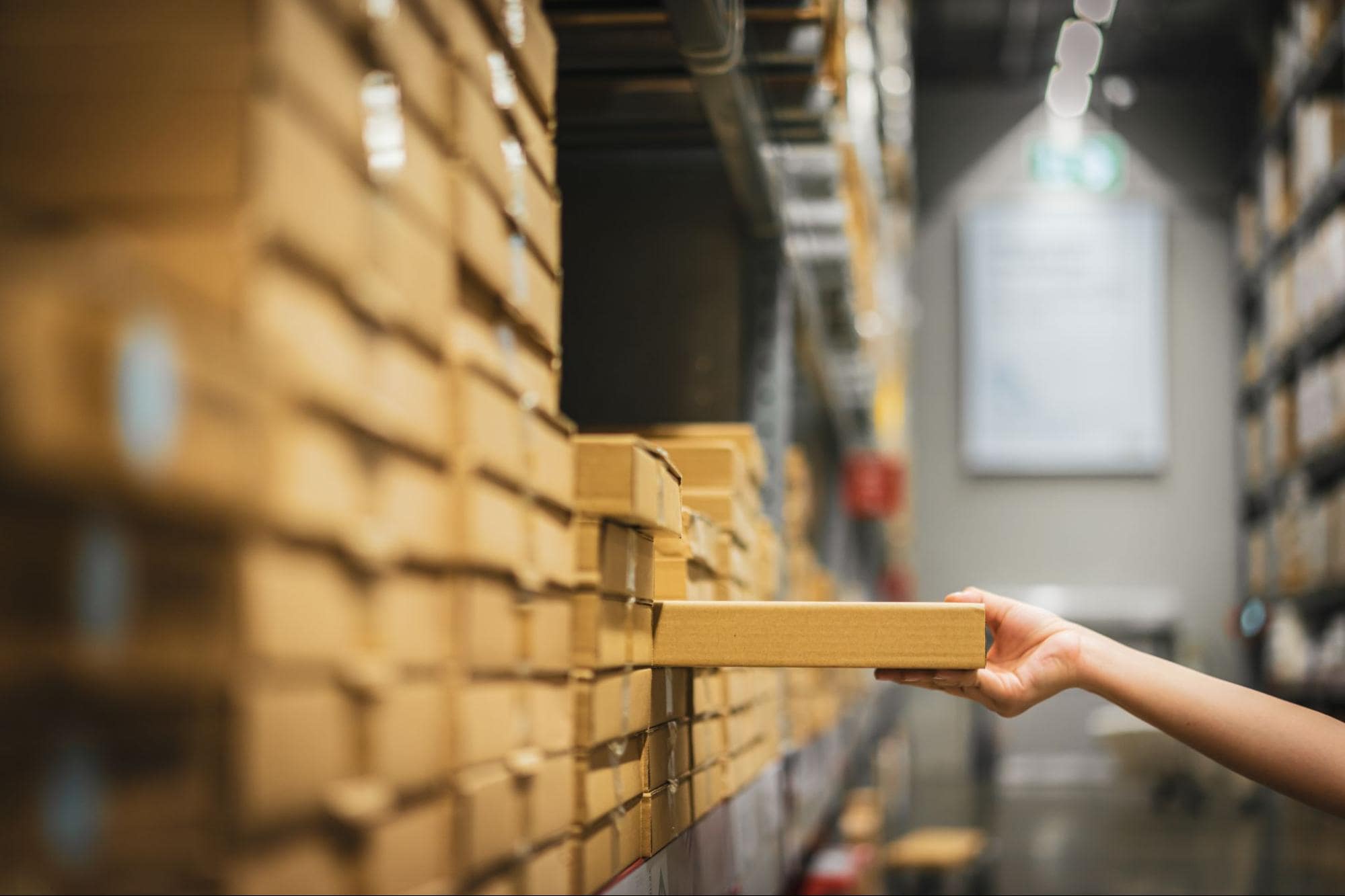 A picture of a hand talking a cardboard box off a shelf in a warehouse.