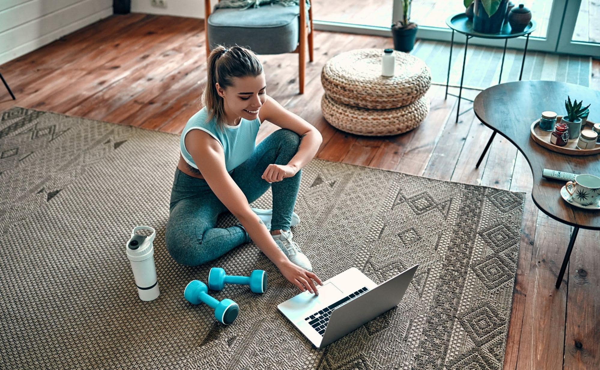 A young woman working out at home using her laptop for home workout videos.