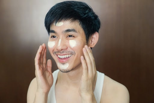 A man with skin care cream on his cheeks, nose, forehead, and chin.