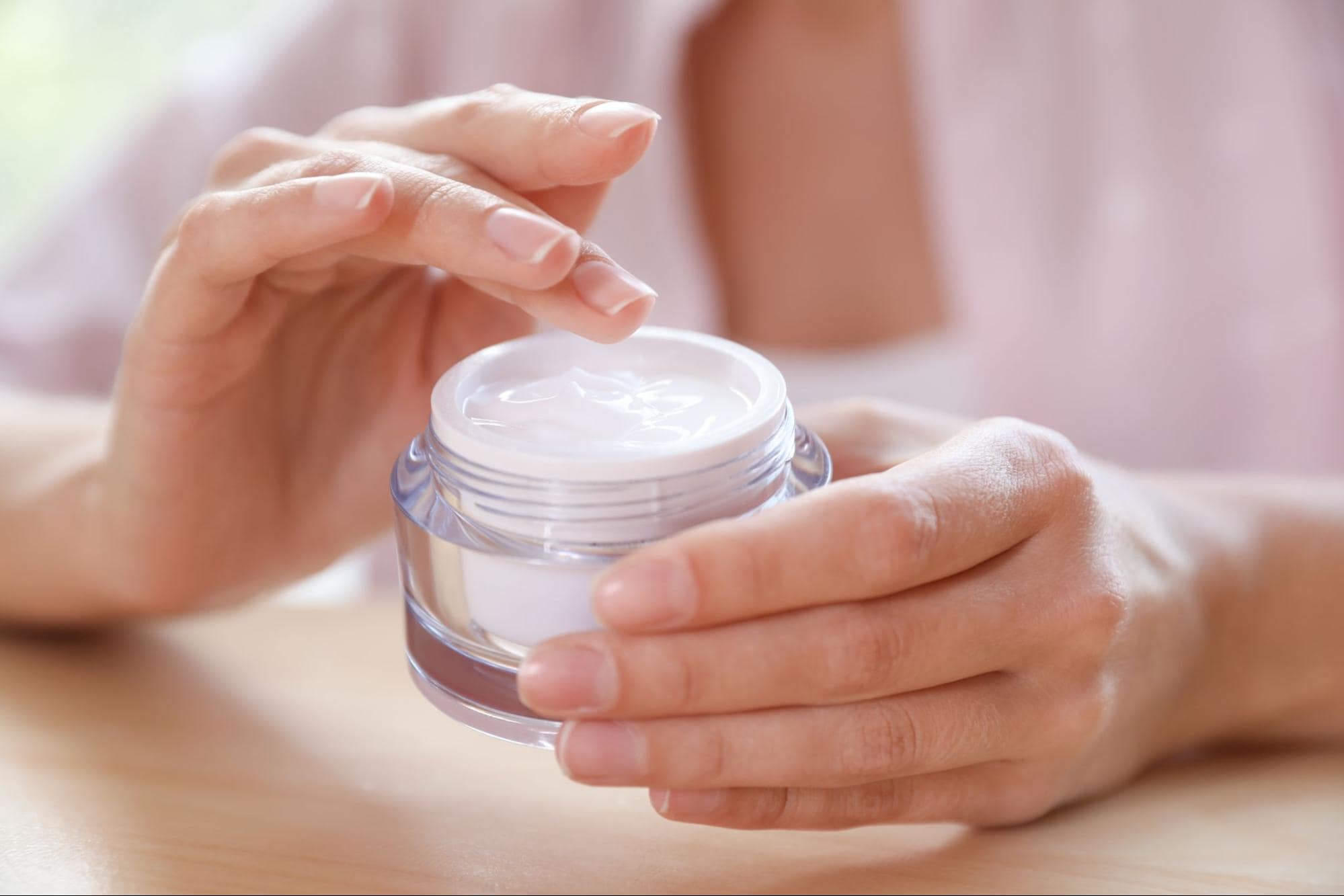 a woman using a facial cream in a glass jar.